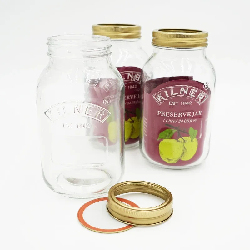 Three Kilner preserving jars with gold lids, two sealed and one open, with spare lid rings in front